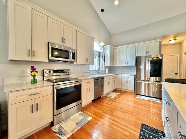 kitchen featuring stainless steel appliances, white cabinetry, decorative light fixtures, and light hardwood / wood-style flooring