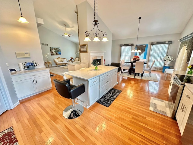 kitchen featuring ceiling fan with notable chandelier, stainless steel electric range, light hardwood / wood-style flooring, white cabinets, and pendant lighting