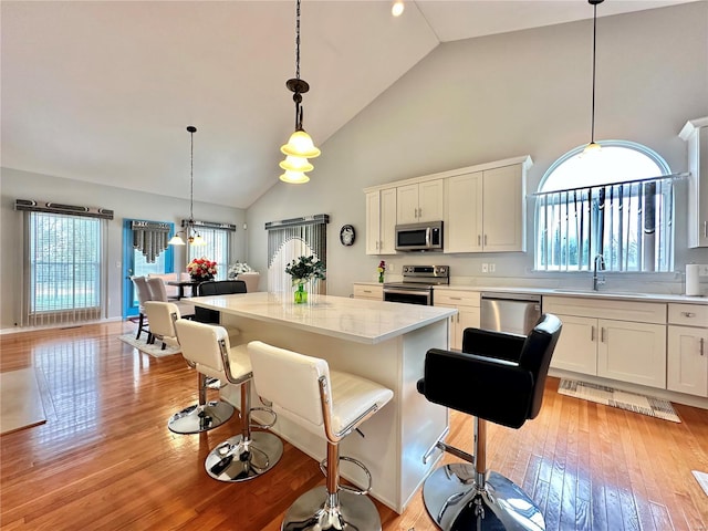 kitchen with stainless steel appliances, a wealth of natural light, a kitchen island, and high vaulted ceiling