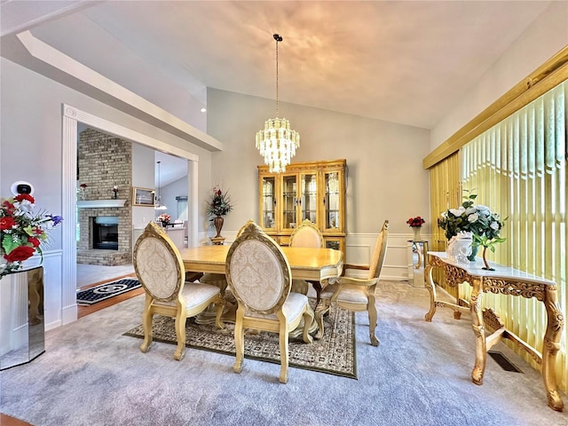 dining space featuring a chandelier, lofted ceiling, carpet, and a brick fireplace