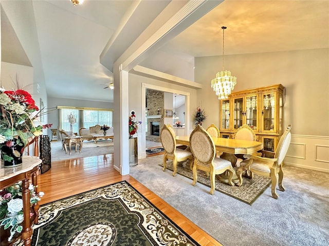 dining area featuring lofted ceiling, hardwood / wood-style floors, ceiling fan with notable chandelier, and a brick fireplace