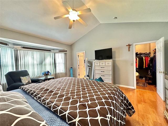 bedroom with ceiling fan, a walk in closet, a closet, light wood-type flooring, and vaulted ceiling