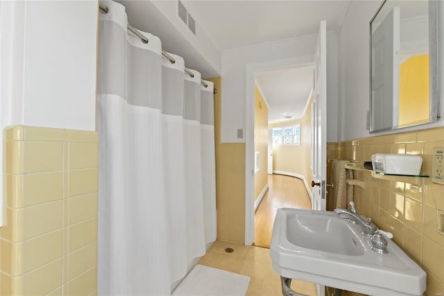 bathroom with tile patterned floors, tile walls, crown molding, and sink