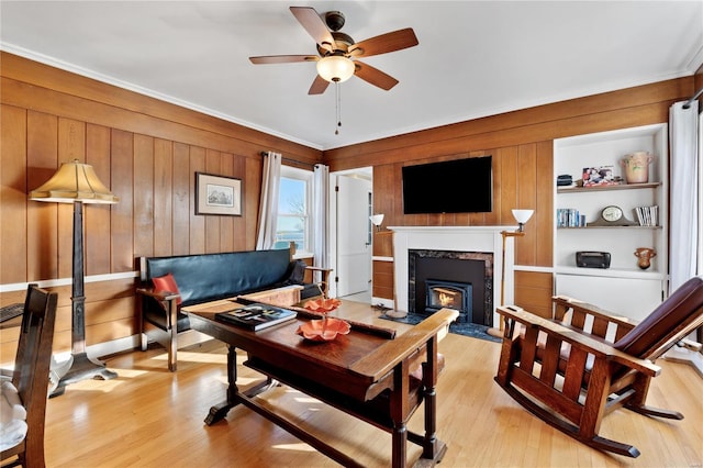 living room featuring built in shelves, light hardwood / wood-style flooring, wooden walls, and a premium fireplace