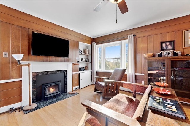 living room with wood walls, built in features, ceiling fan, and light wood-type flooring