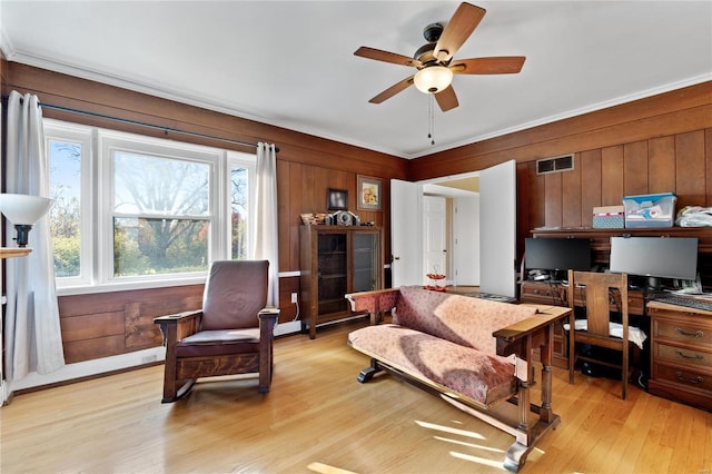 interior space with ornamental molding, light wood-type flooring, ceiling fan, and wooden walls