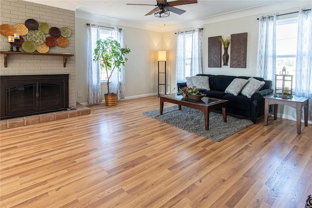 living room featuring ceiling fan, crown molding, light hardwood / wood-style floors, and a brick fireplace