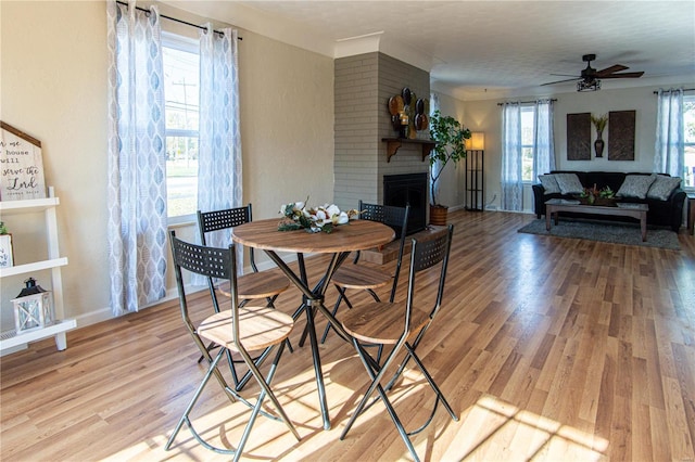 dining room with a brick fireplace, light hardwood / wood-style flooring, and plenty of natural light