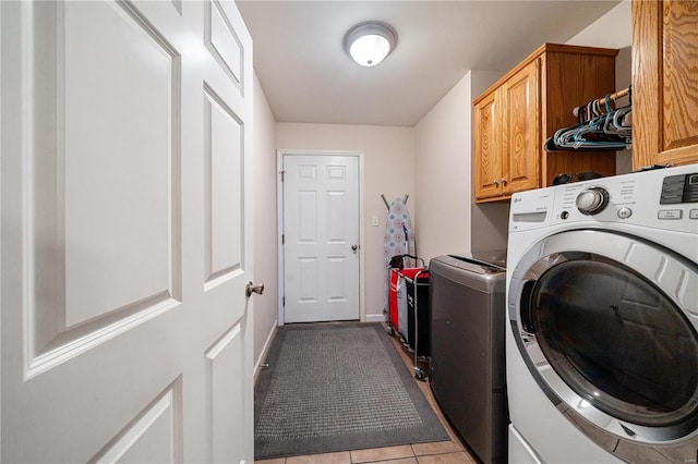 laundry area featuring separate washer and dryer, light tile patterned floors, and cabinets