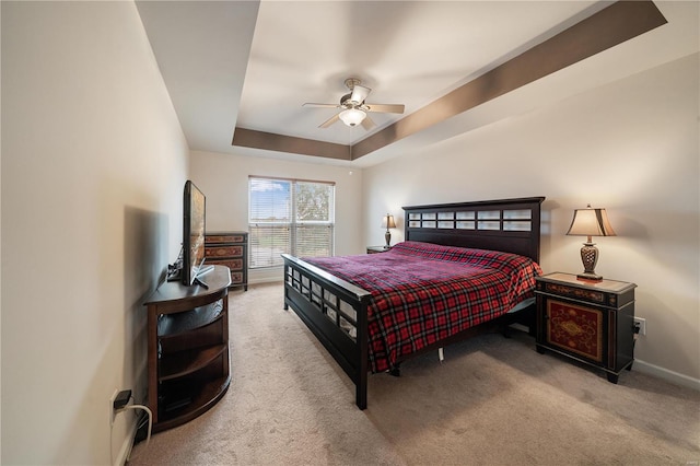 carpeted bedroom with a raised ceiling and ceiling fan