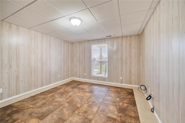 spare room featuring a paneled ceiling and wood walls