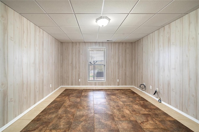 unfurnished room with tile patterned flooring, a paneled ceiling, and wood walls