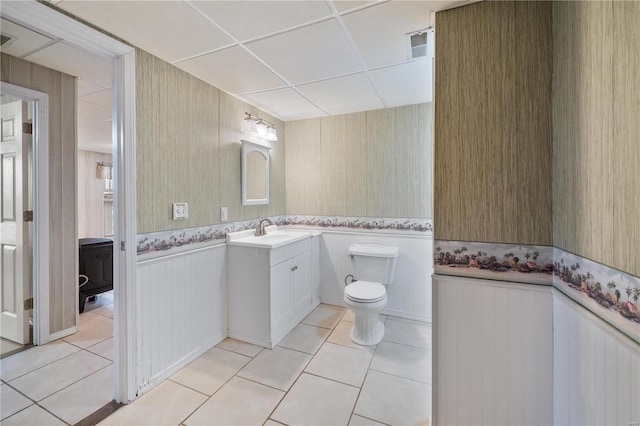 bathroom with toilet, vanity, tile patterned floors, and a drop ceiling