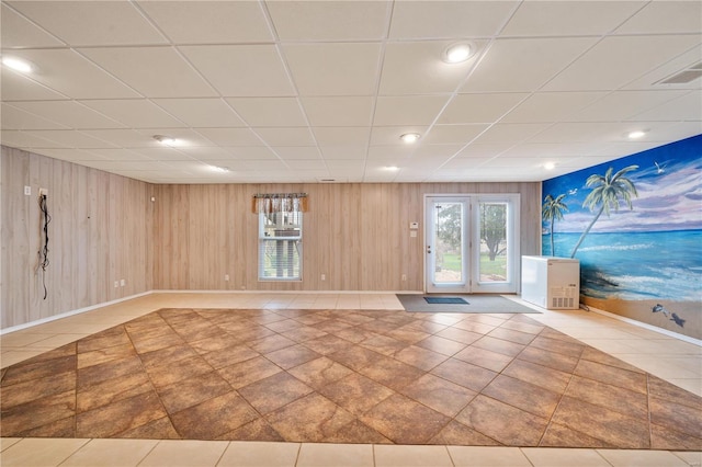 interior space with tile patterned floors, a drop ceiling, and wooden walls