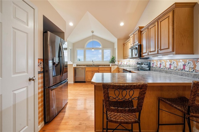 kitchen featuring lofted ceiling, a kitchen breakfast bar, appliances with stainless steel finishes, light hardwood / wood-style floors, and kitchen peninsula