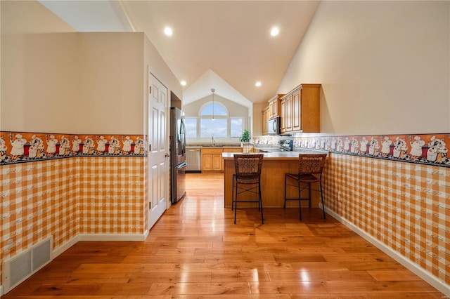 kitchen featuring sink, kitchen peninsula, light wood-type flooring, a kitchen bar, and appliances with stainless steel finishes