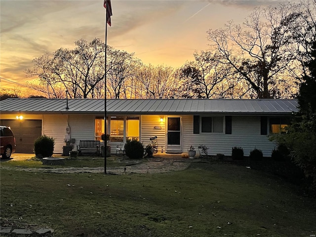 back house at dusk featuring a lawn and a garage