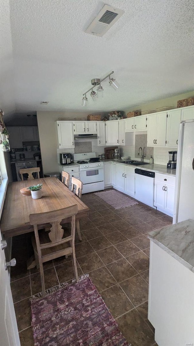 kitchen with white appliances, white cabinetry, a textured ceiling, and dark tile patterned flooring