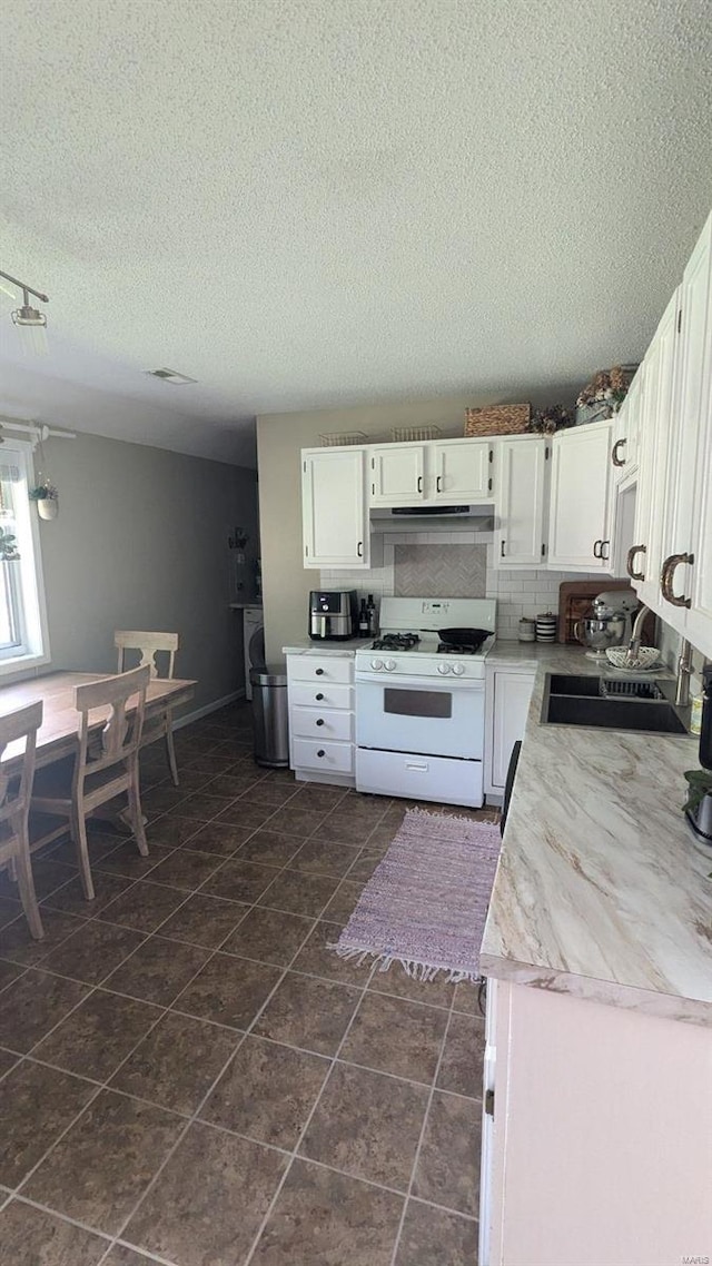 kitchen with dark tile patterned floors, a textured ceiling, white range with gas stovetop, sink, and white cabinets