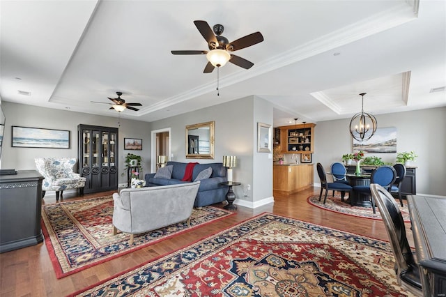 living room featuring ceiling fan with notable chandelier, crown molding, dark wood-type flooring, and a tray ceiling