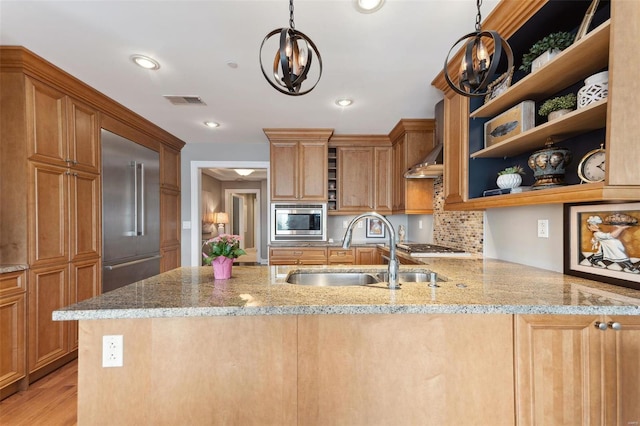 kitchen with sink, hanging light fixtures, light stone counters, kitchen peninsula, and built in appliances