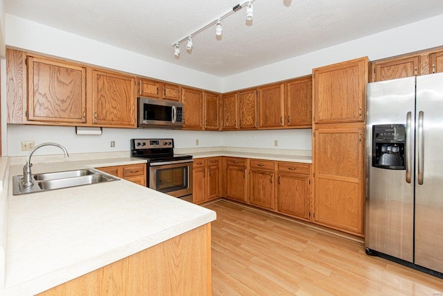 kitchen featuring sink, light hardwood / wood-style floors, track lighting, a textured ceiling, and appliances with stainless steel finishes