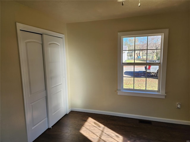 unfurnished bedroom with dark hardwood / wood-style flooring, a closet, and multiple windows