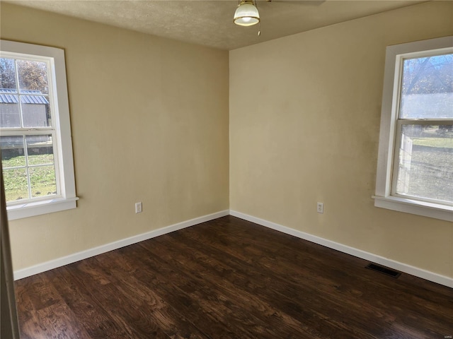 empty room with dark hardwood / wood-style flooring, ceiling fan, a textured ceiling, and a healthy amount of sunlight