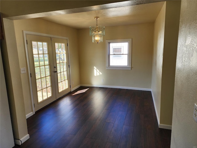 spare room with dark wood-type flooring, french doors, and a notable chandelier