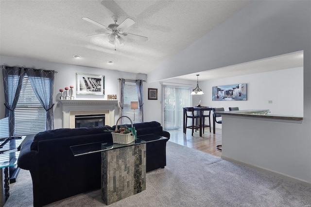 carpeted living room featuring ceiling fan with notable chandelier, a textured ceiling, vaulted ceiling, and a wealth of natural light