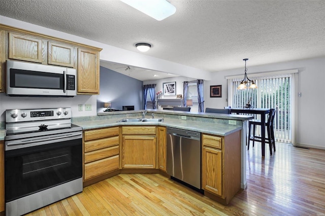 kitchen with light wood-type flooring, kitchen peninsula, sink, and appliances with stainless steel finishes