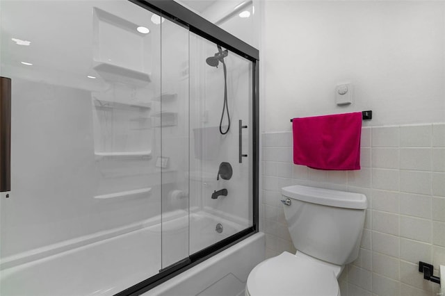 bathroom featuring bath / shower combo with glass door, tile walls, and toilet