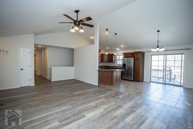 unfurnished living room featuring ceiling fan with notable chandelier, light hardwood / wood-style floors, and vaulted ceiling