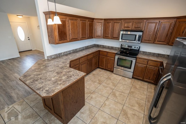 kitchen featuring kitchen peninsula, appliances with stainless steel finishes, light wood-type flooring, and decorative light fixtures