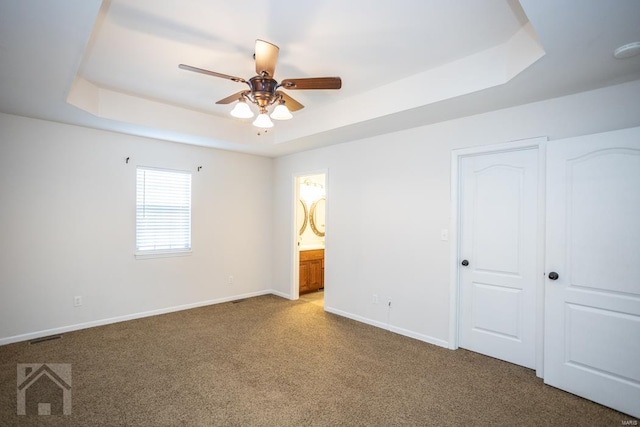 unfurnished bedroom featuring carpet flooring, a tray ceiling, ensuite bath, and ceiling fan