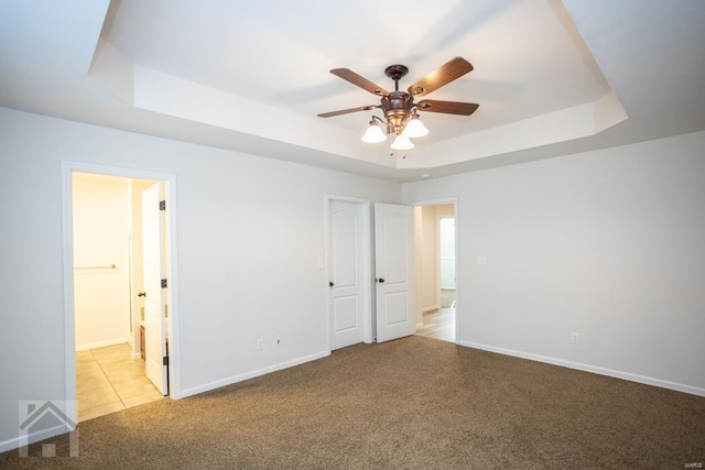 unfurnished bedroom featuring ceiling fan, a closet, light colored carpet, and a tray ceiling