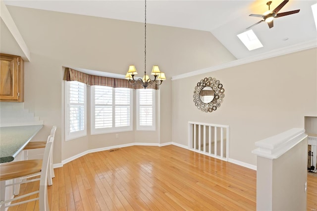 unfurnished dining area featuring vaulted ceiling with skylight, ceiling fan with notable chandelier, and light wood-type flooring