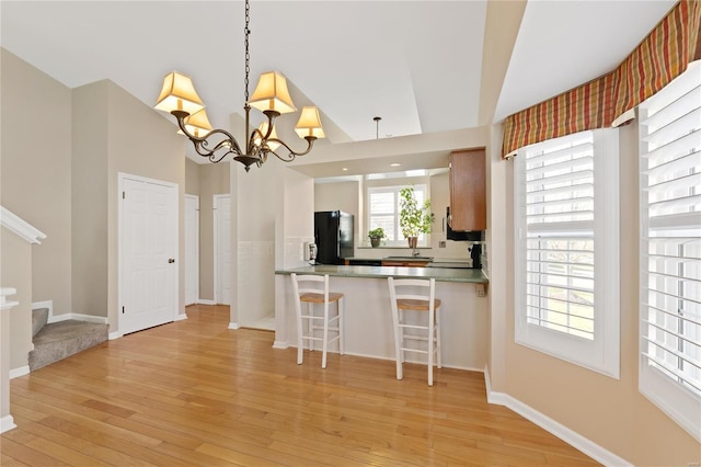 kitchen with a kitchen breakfast bar, kitchen peninsula, pendant lighting, light hardwood / wood-style floors, and black refrigerator