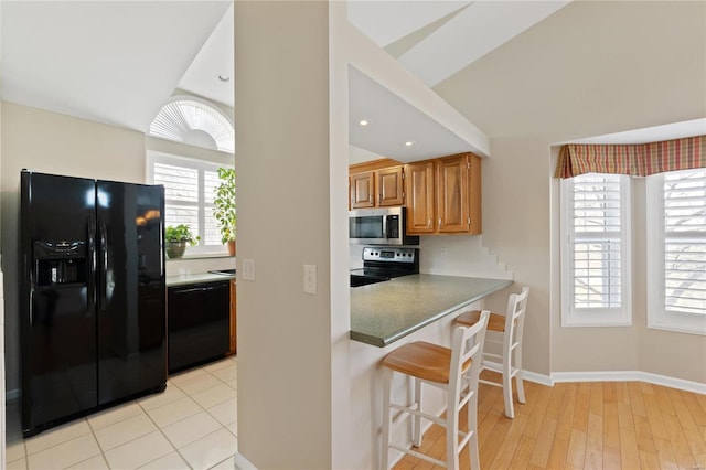 kitchen featuring black appliances, a kitchen bar, kitchen peninsula, and light hardwood / wood-style flooring