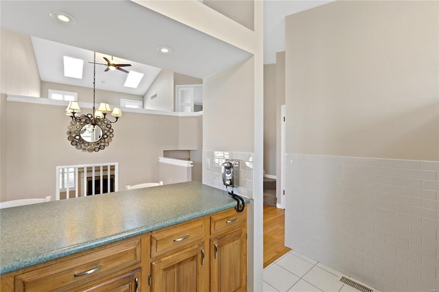 kitchen featuring ceiling fan with notable chandelier, light wood-type flooring, and lofted ceiling with skylight