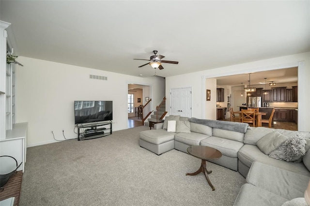 living area featuring stairs, ceiling fan with notable chandelier, carpet, and visible vents