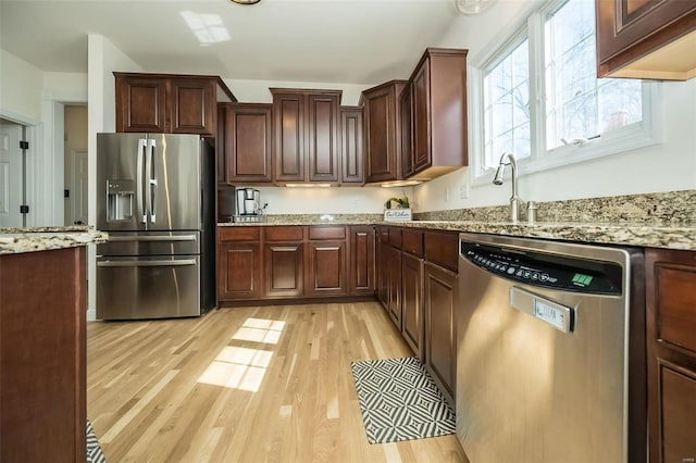 kitchen with light wood finished floors, dark brown cabinetry, light stone counters, stainless steel appliances, and a sink