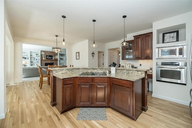 kitchen with a center island, stainless steel appliances, light wood-type flooring, and light stone countertops