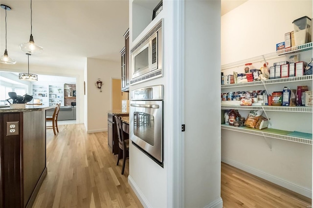 kitchen featuring light wood finished floors, dark brown cabinetry, decorative light fixtures, light stone counters, and stainless steel appliances