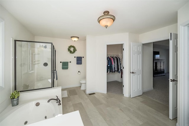 bathroom with a walk in closet, toilet, a stall shower, baseboards, and a whirlpool tub