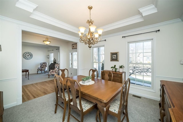 dining space with an inviting chandelier, visible vents, a tray ceiling, and ornamental molding