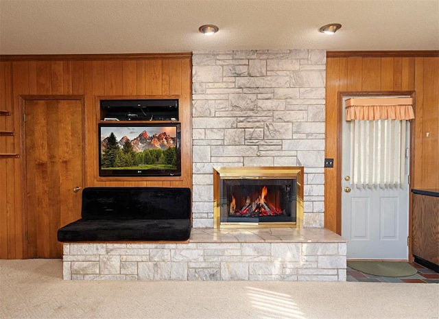 carpeted living room with ornamental molding, a fireplace, a textured ceiling, and wooden walls