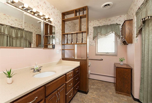 bathroom featuring toilet, tile walls, a textured ceiling, baseboard heating, and vanity