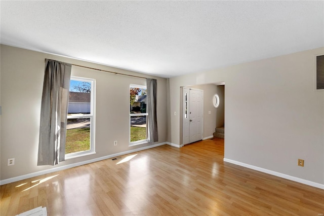 spare room with a healthy amount of sunlight, a textured ceiling, and light hardwood / wood-style flooring