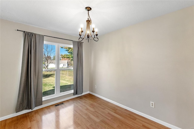 unfurnished room with hardwood / wood-style floors, a healthy amount of sunlight, and an inviting chandelier